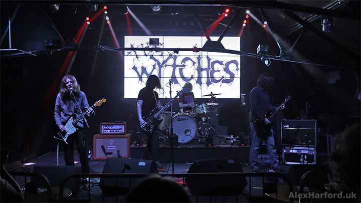 Wytches onstage with their logo on a bright screen behind them.